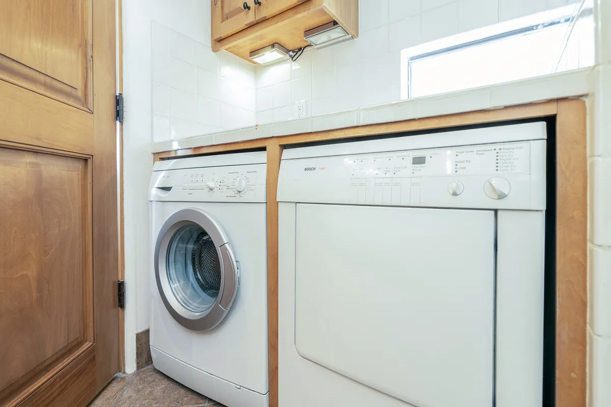 A dedicated laundry area featuring a modern washer and dryer, set within wooden cabinetry. The space is organized and designed for efficiency, with supplies neatly arranged for easy use.