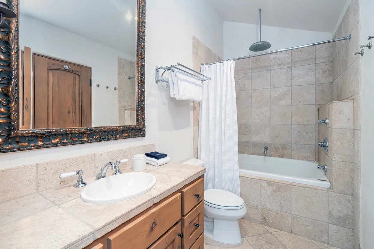 A modern bathroom featuring a large ornate mirror, a bathroom sink, a bathtub with a shower, and warm wooden cabinetry. The space radiates calm and serenity, inviting guests to unwind and indulge in self-care routines.
