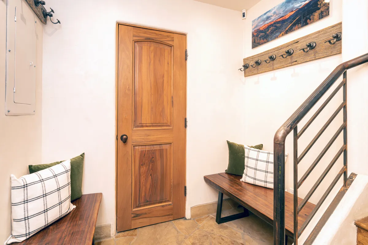A welcoming entryway/mudroom with wooden doors, bench seating for removing shoes or boots, and decorative hooks for coats and gear. Artwork on the wall adds a cozy touch.